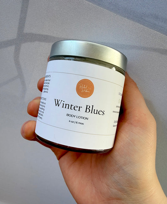 Hand holding a jar of 'Winter Blues' body lotion with a plain background
