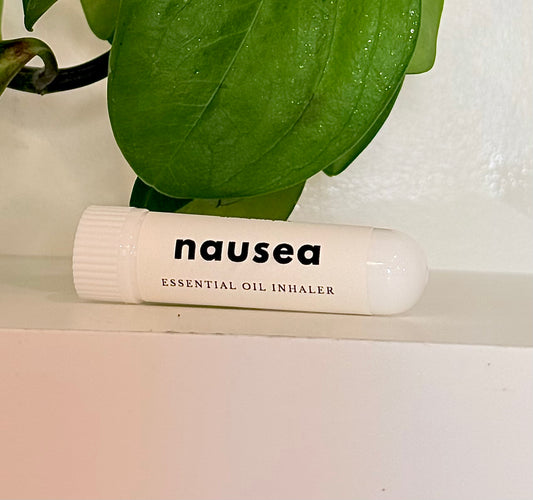Essential oil inhaler labeled 'nausea' on a white surface with green leaves in the background