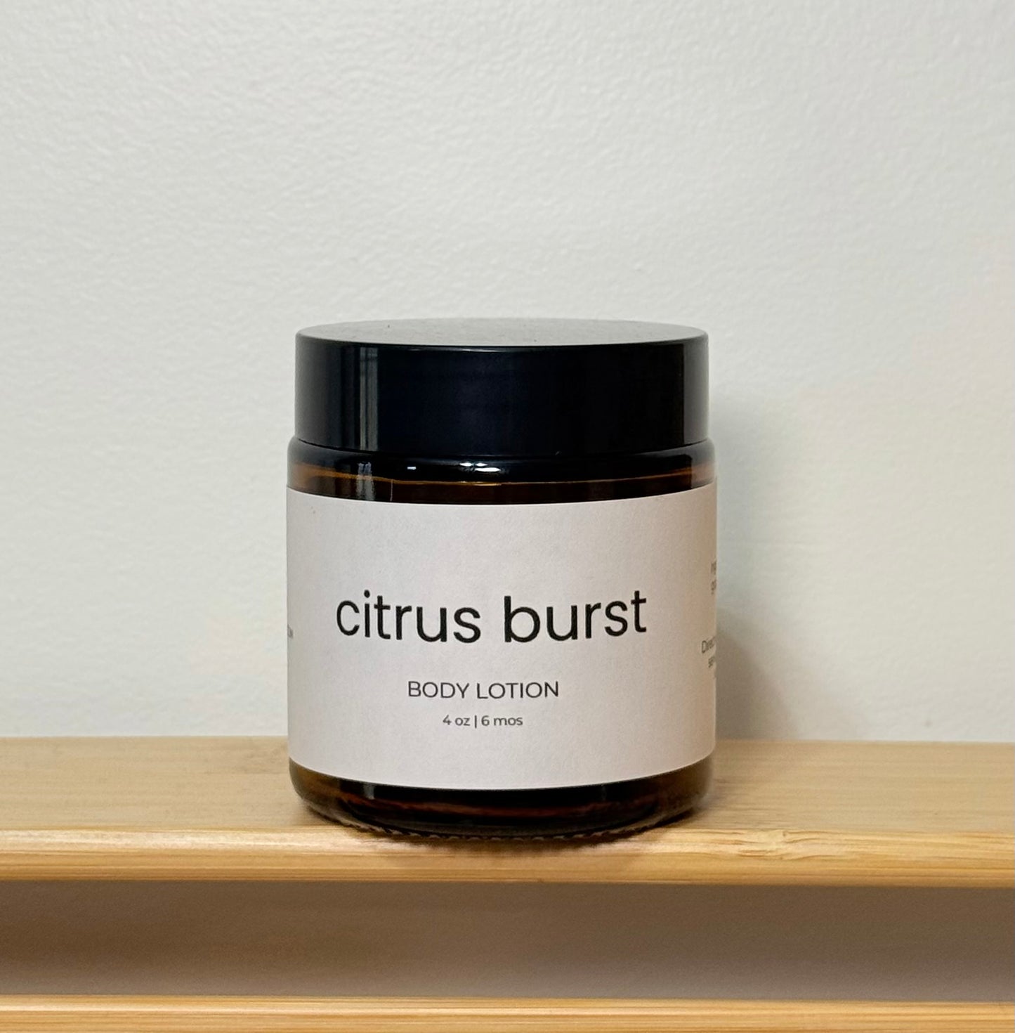 Jar of 'citrus burst' body lotion on a wooden shelf with a light gray background