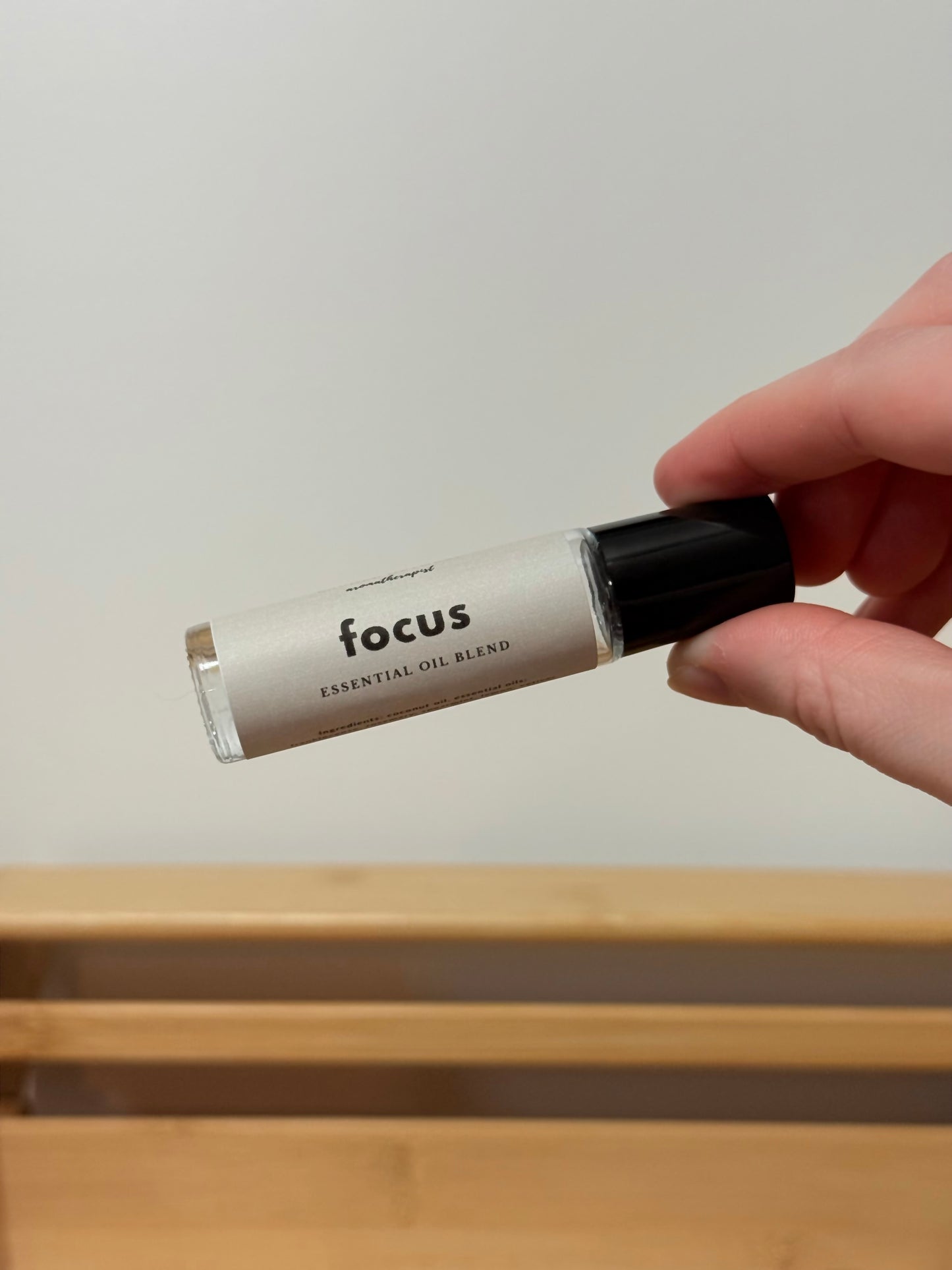 Hand holding a bottle labeled 'focus' on a wooden surface with a neutral background