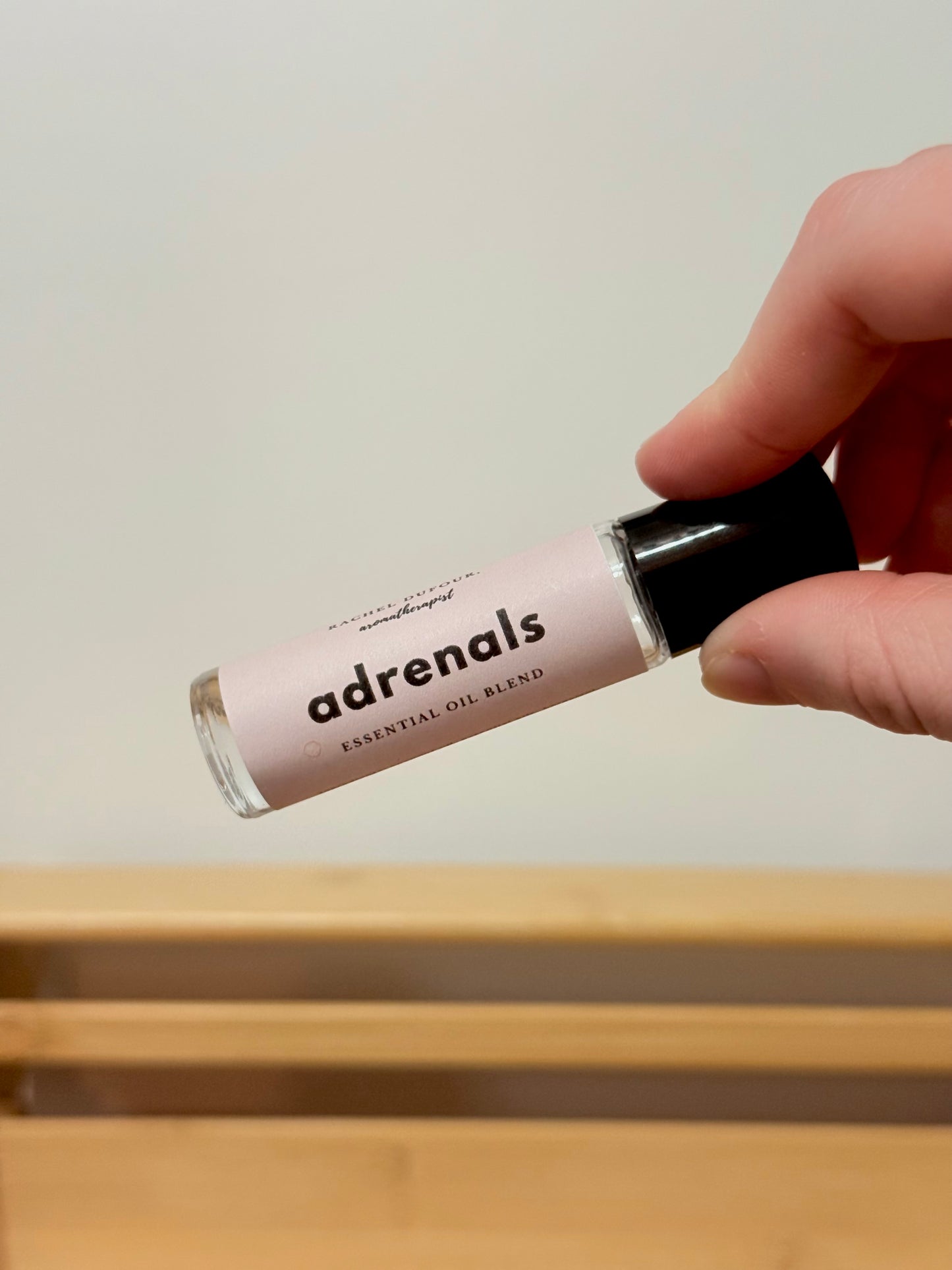 Hand holding a small rollerball bottle labeled 'adrenals' against a neutral background