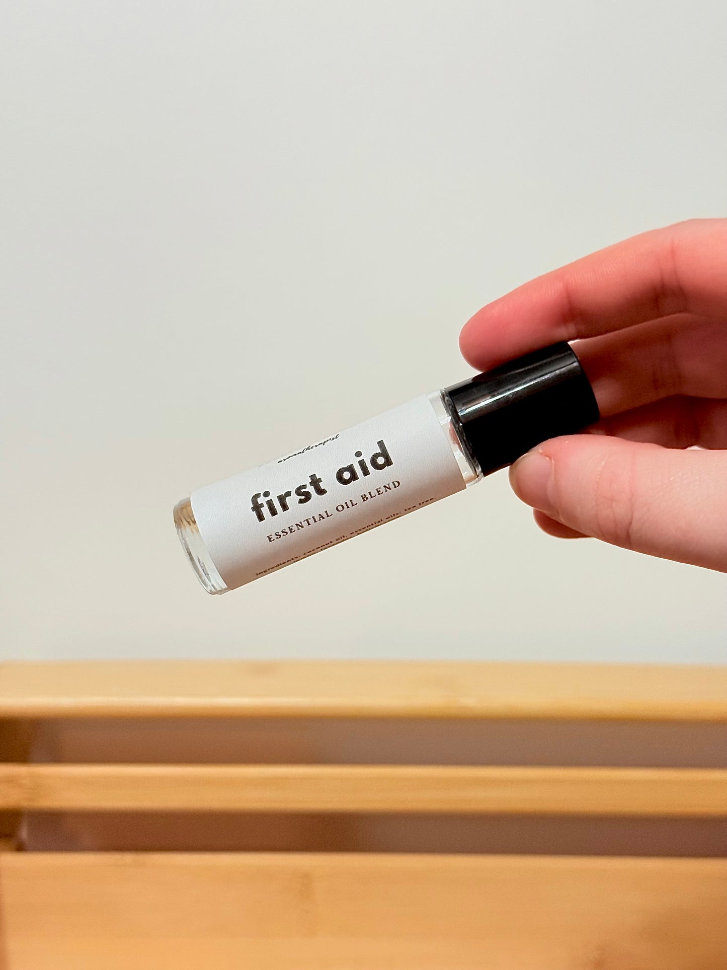 Hand holding a small rollerball bottle labeled 'first aid' against a plain background