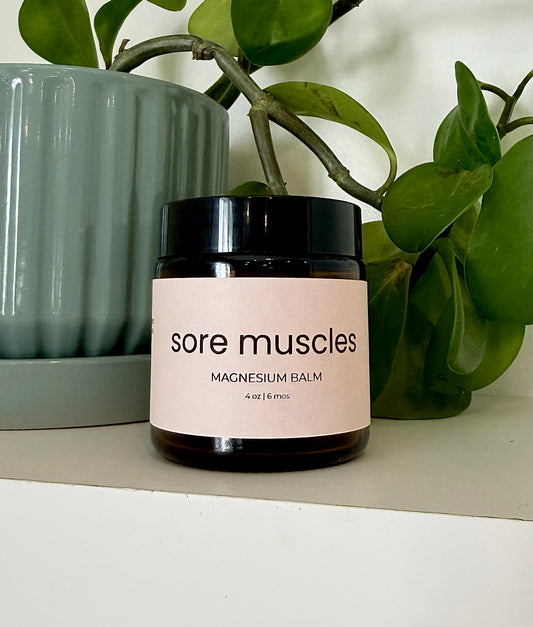 Jar of magnesium balm labeled 'sore muscles' on a surface with plants in the background