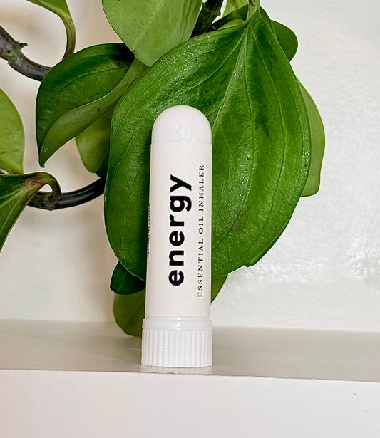 White essential oil Inhaler labeled 'energy' with green leaves in the background