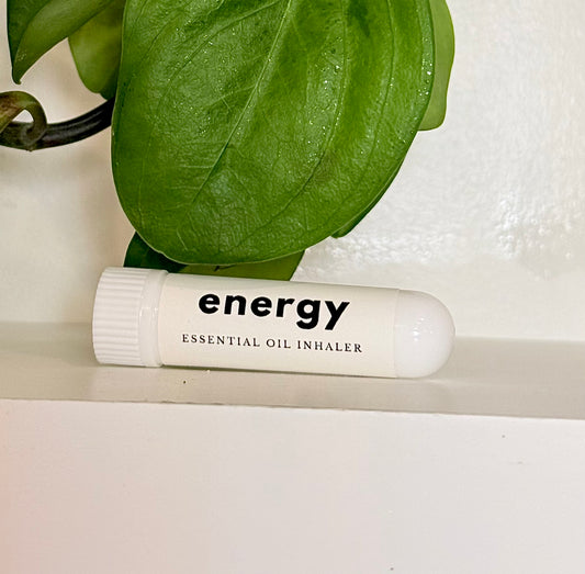 Essential oil inhaler labeled 'energy' on a white surface with green leaves in the background
