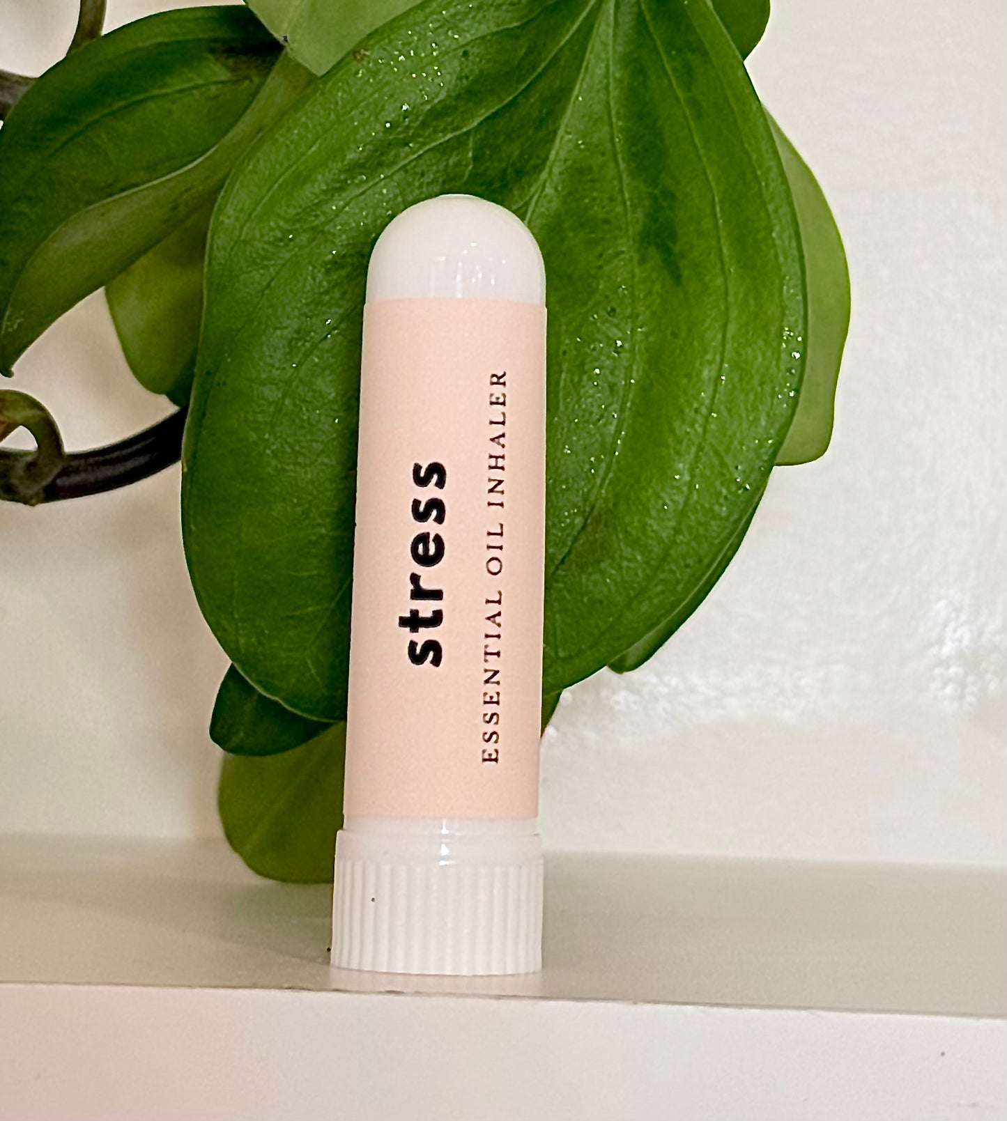 Essential oil Inhaler labeled 'stress' on a white surface with green leaves in the background