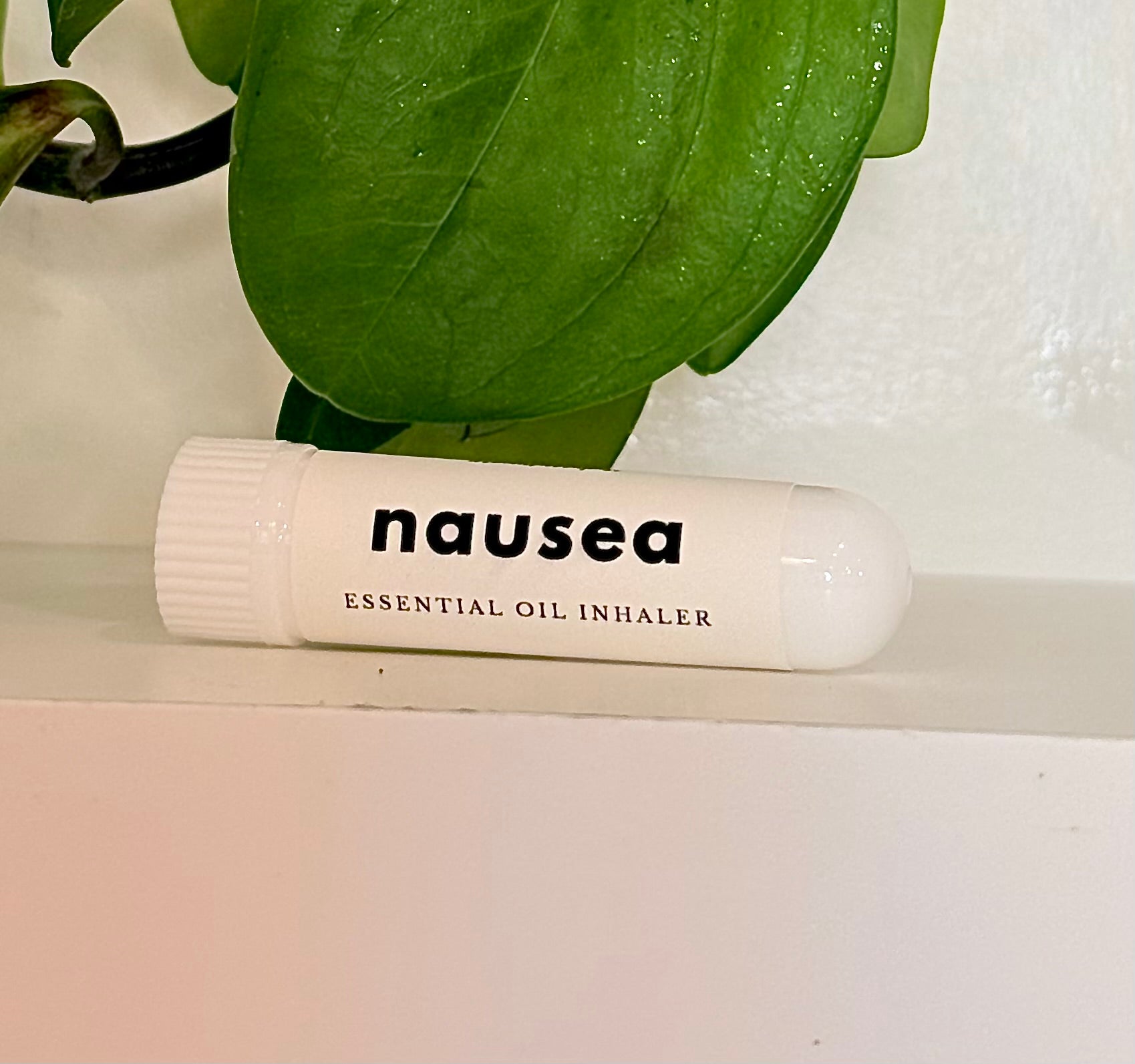 Essential oil inhaler labeled 'nausea' on a white surface with green leaves in the background