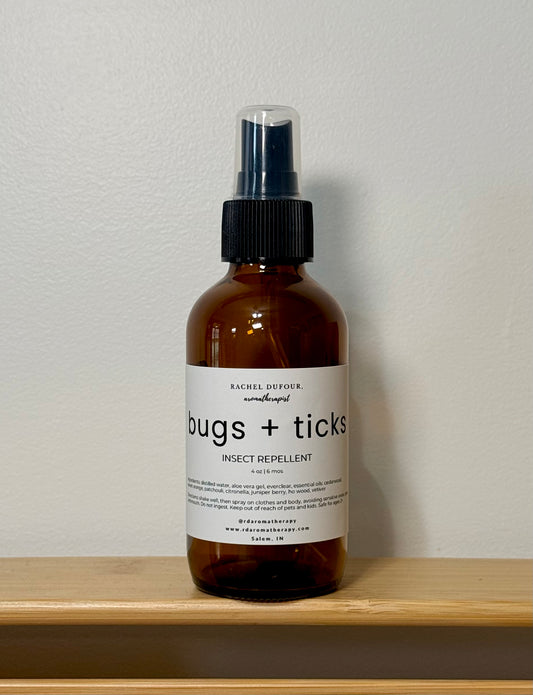 Brown spray bottle labeled 'bugs + ticks' on a wooden surface with a white background