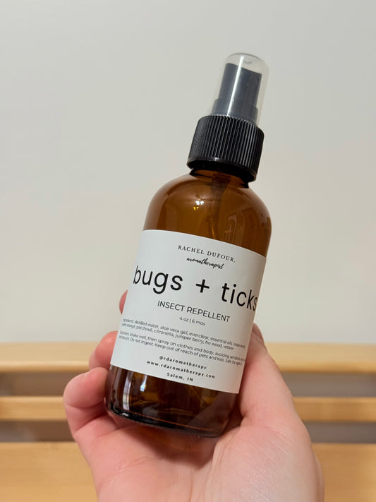 Bottle of 'bugs + ticks' insect repellent held by a hand against a neutral background