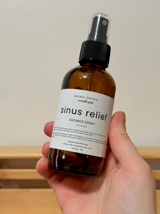 Hand holding a bottle of 'sinus relief' shower spray with a plain background