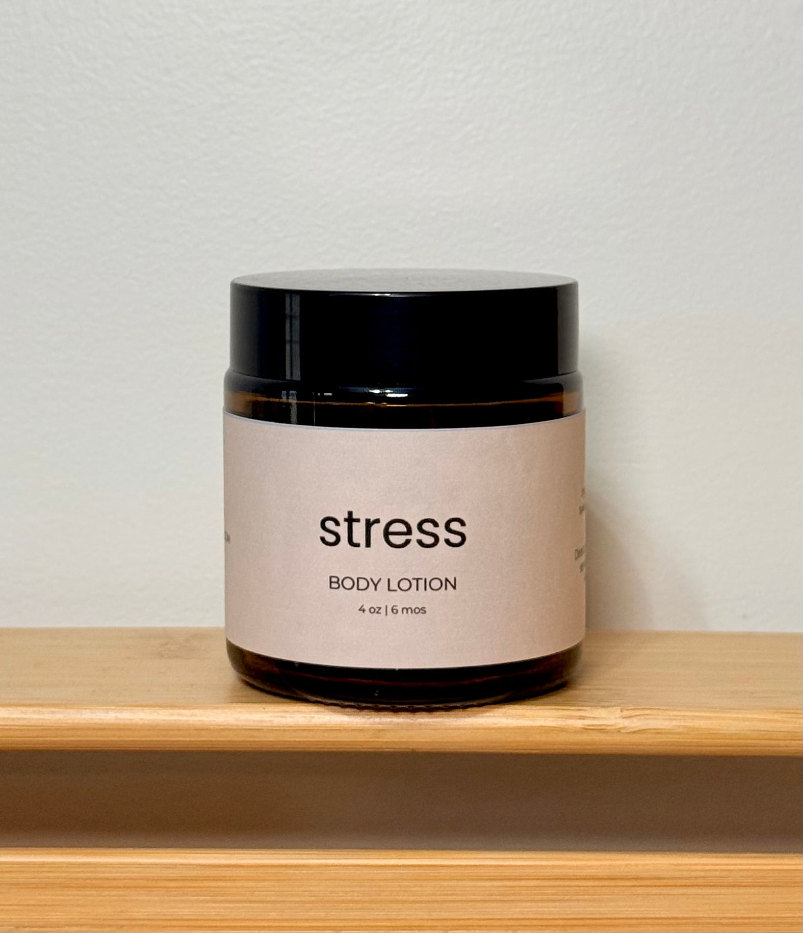 Jar of body lotion labeled 'stress' on a wooden shelf with a light gray background
