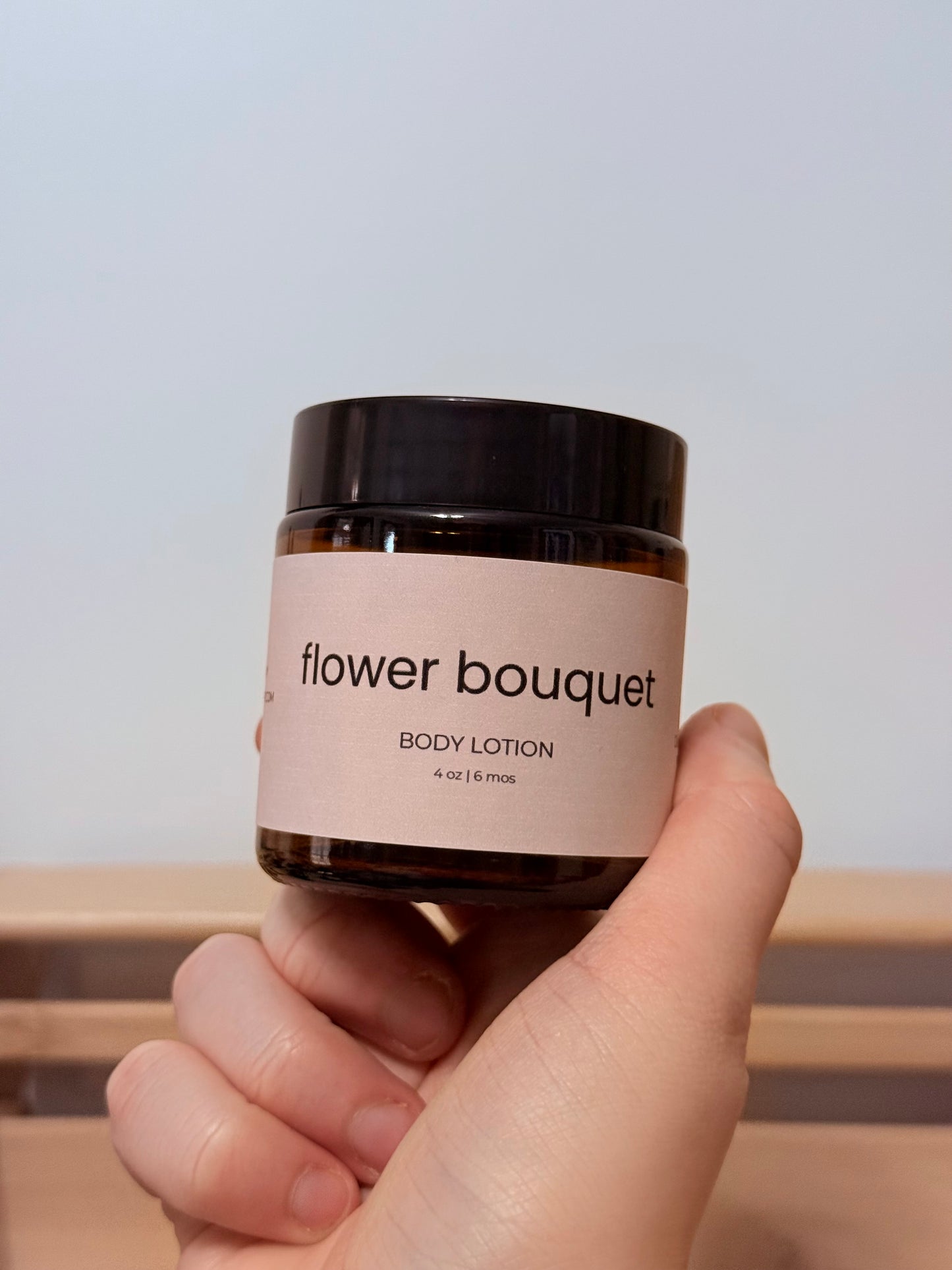 Hand holding a jar of 'flower bouquet' body lotion against a neutral background
