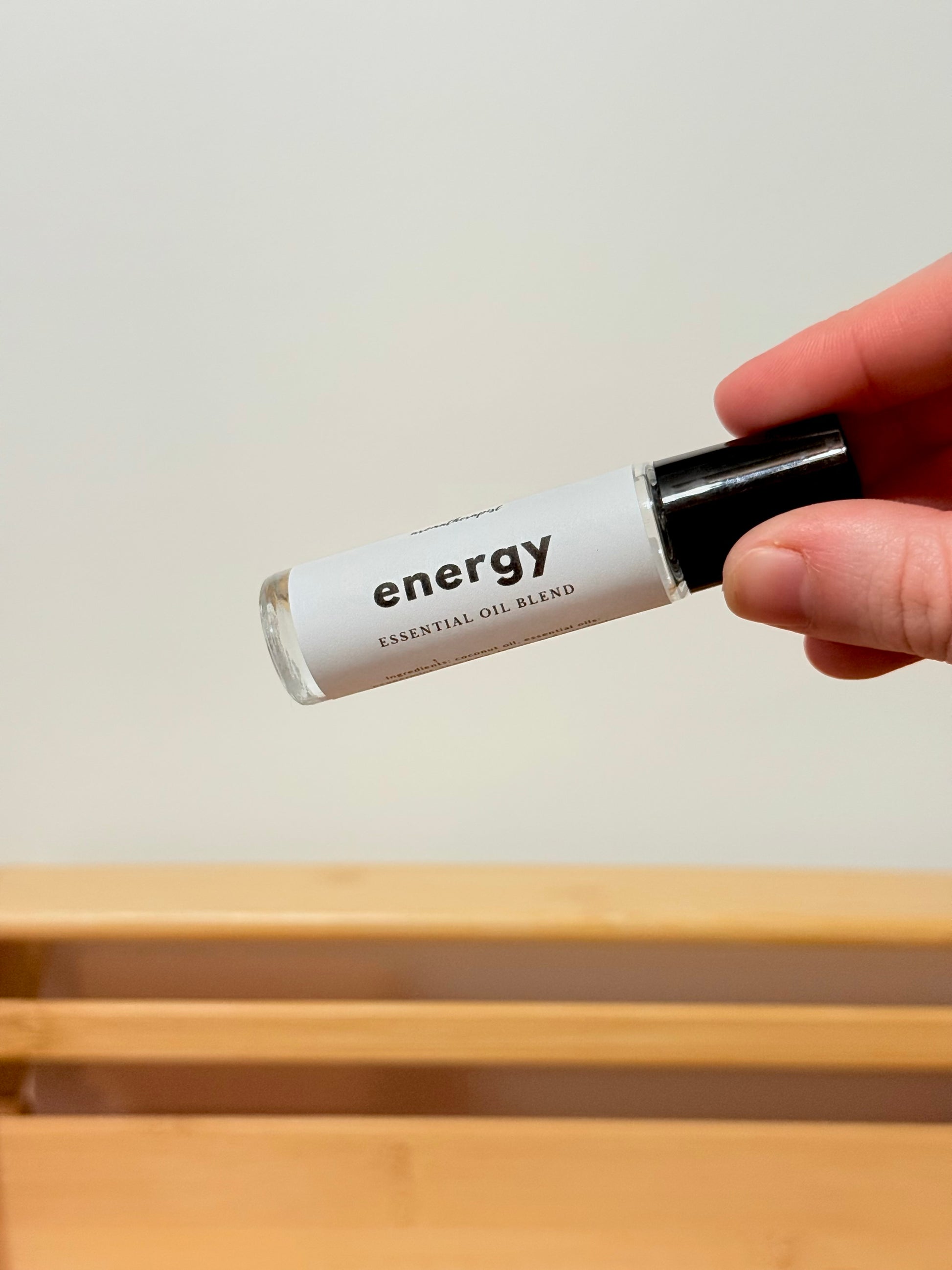 Hand holding a small rollerball labeled 'energy' over a wooden surface.