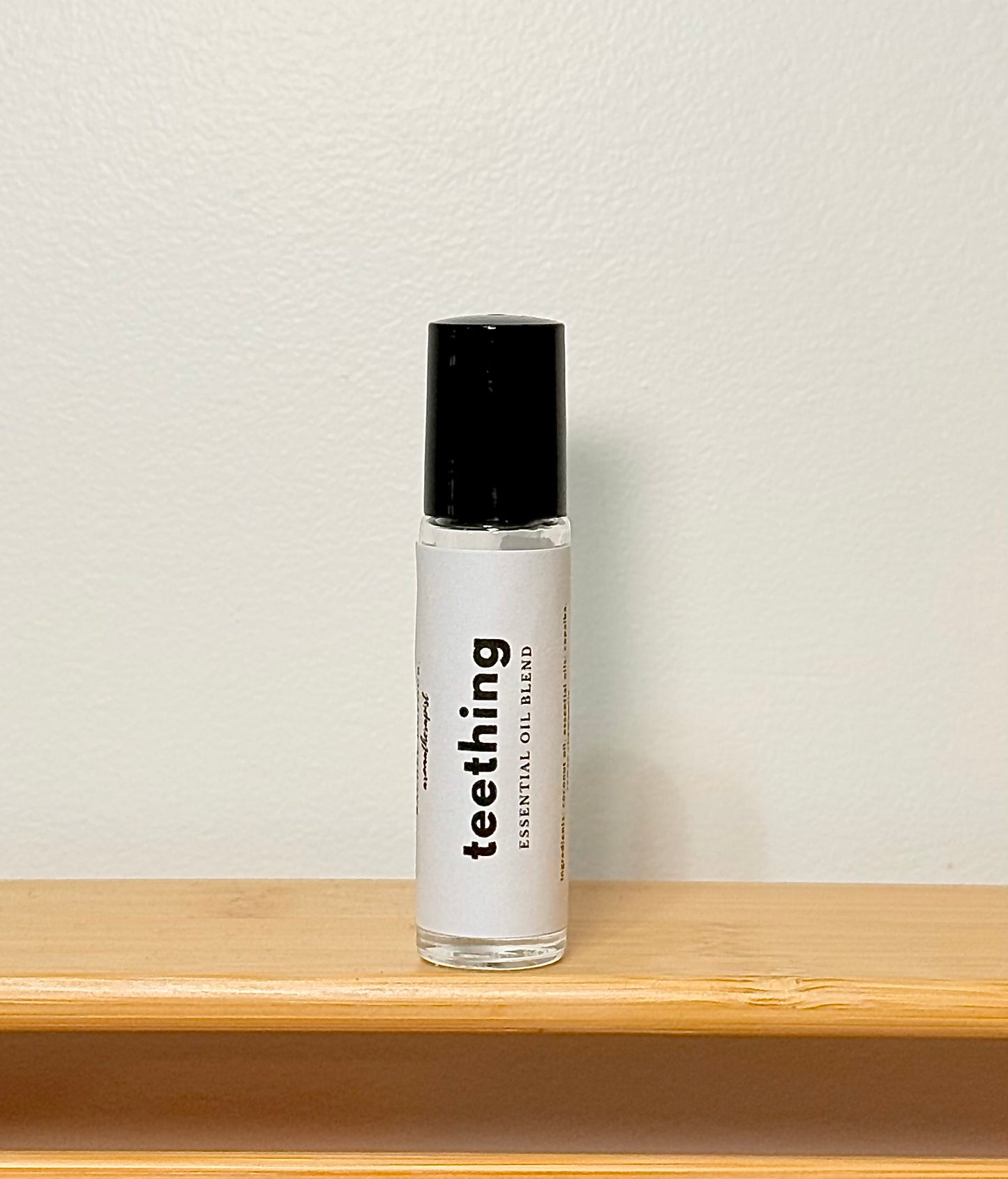 Bottle of 'teething' essential oil blend on a wooden shelf with a light gray background