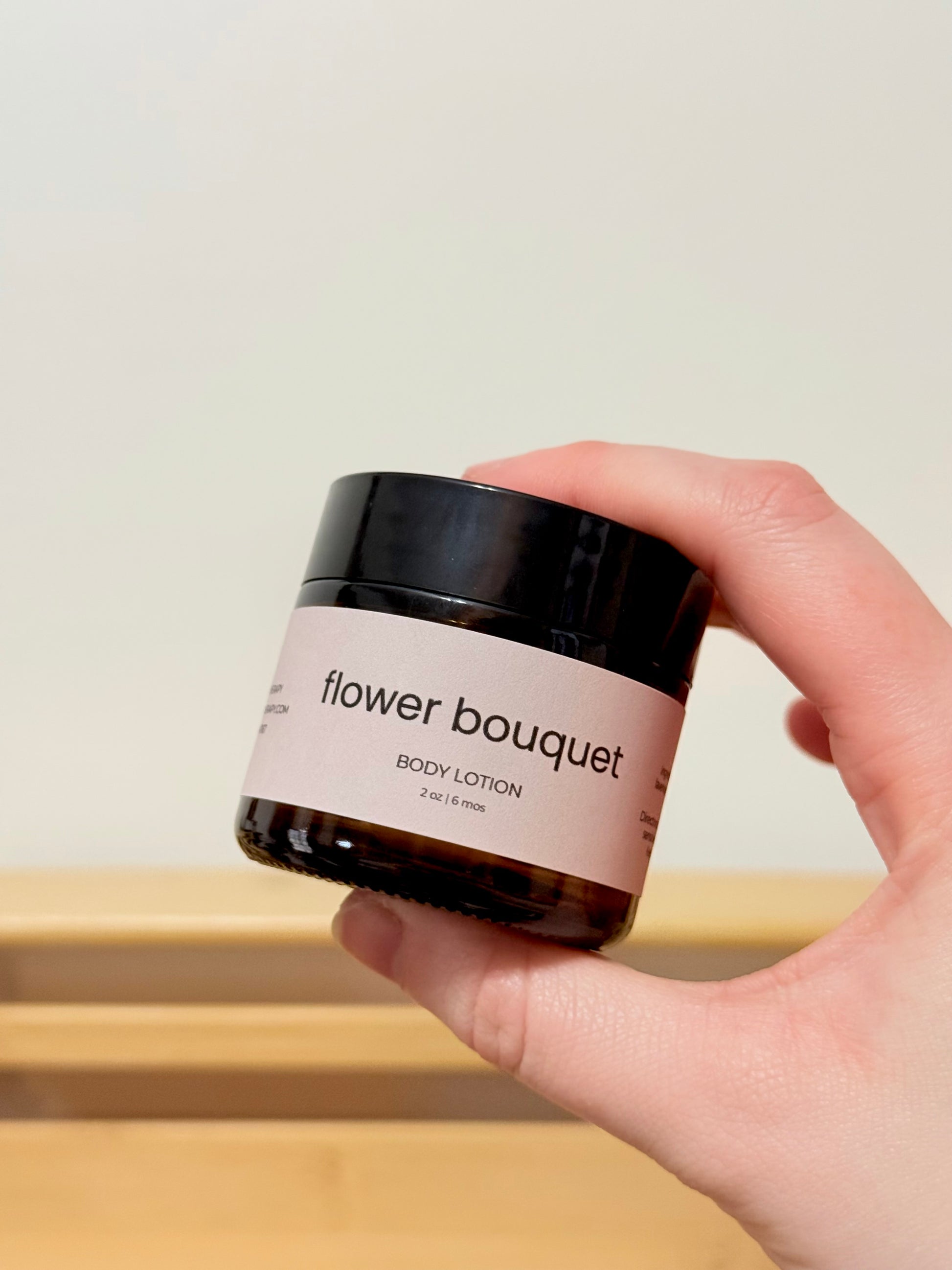 Hand holding a jar of 'flower bouquet' body lotion against a neutral background