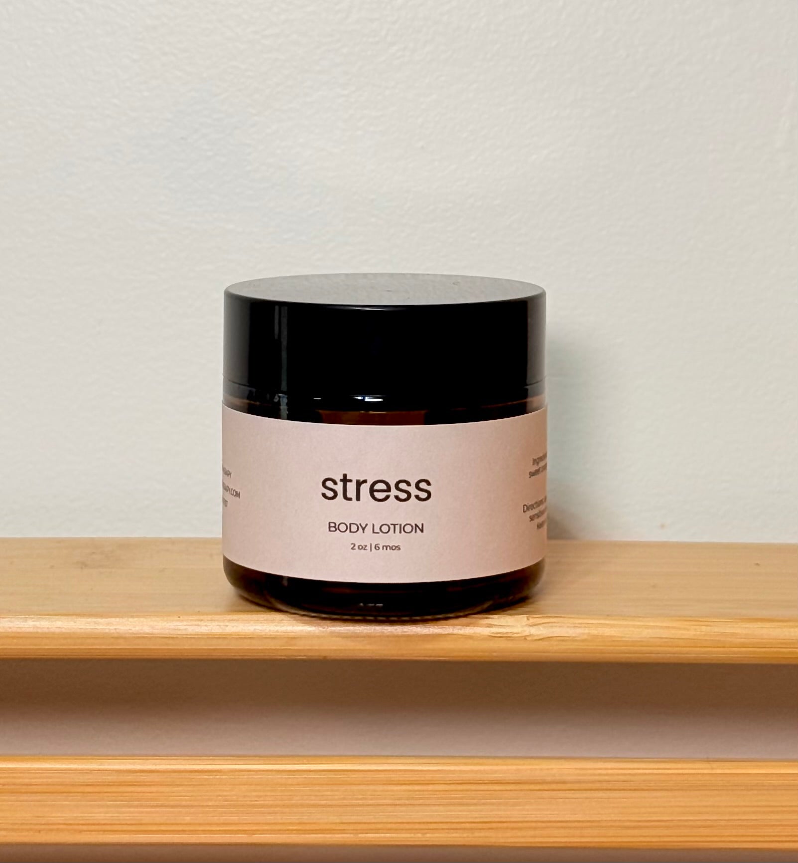 Jar of body lotion labeled 'stress' on a wooden shelf with a neutral background