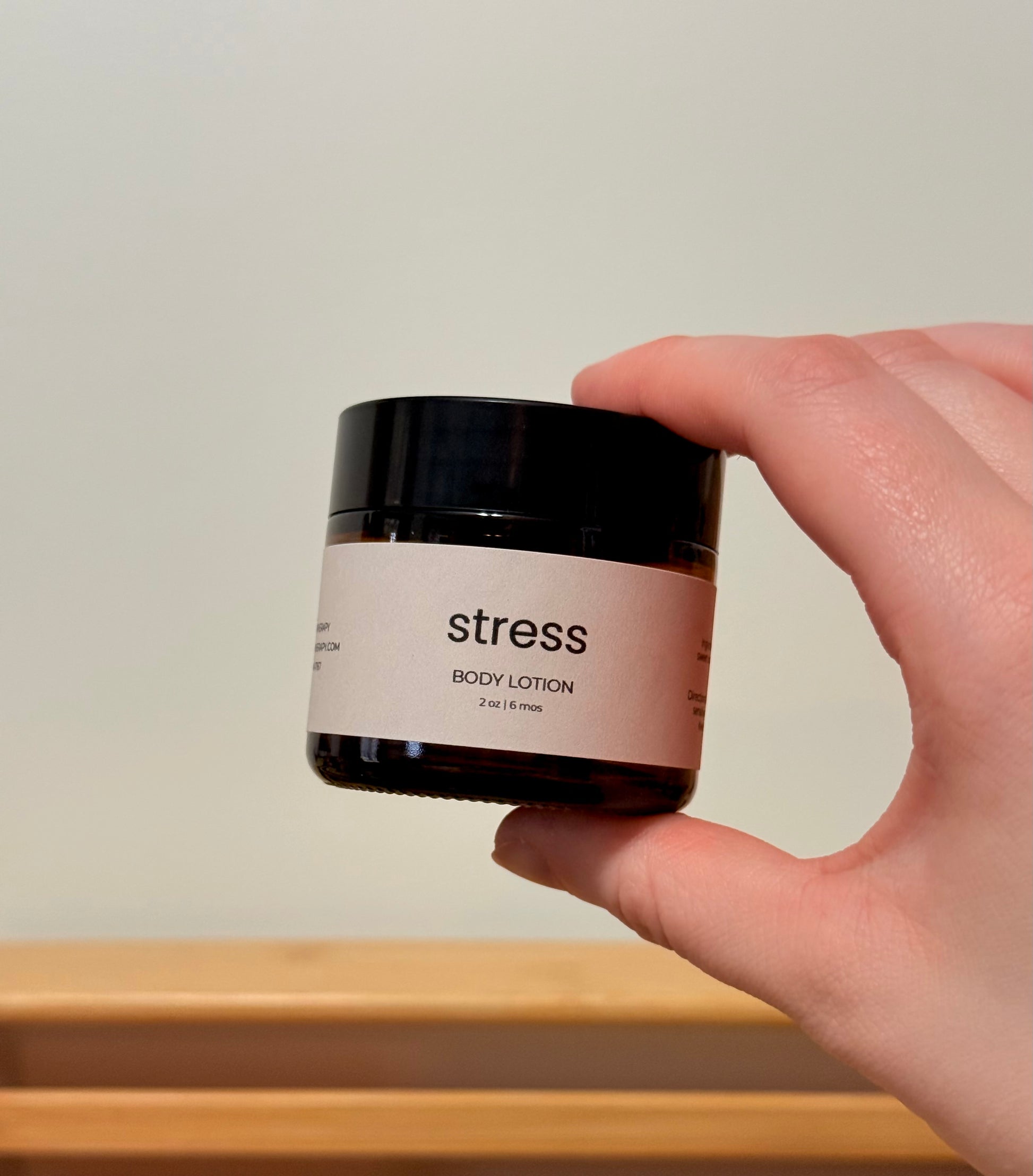 Hand holding a jar of 'stress' body lotion with a plain background