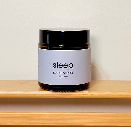 Jar of sleep sugar scrub on a wooden shelf with a neutral background