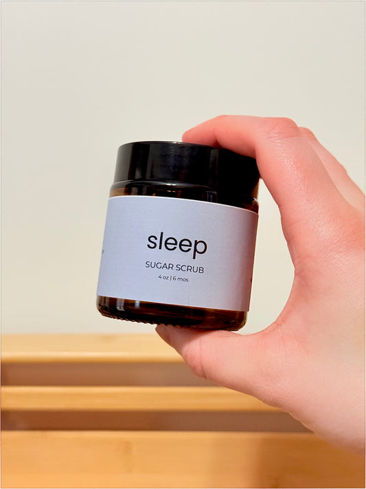 Hand holding a jar of 'sleep' sugar scrub against a neutral background