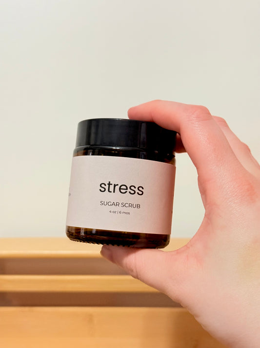 Hand holding a jar of 'stress' sugar scrub with a plain background