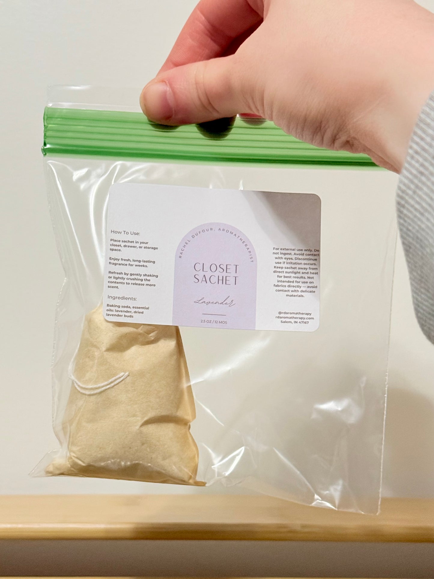 Hand holding a clear plastic bag with a closet sachet labeled 'Lavender' on a white background.