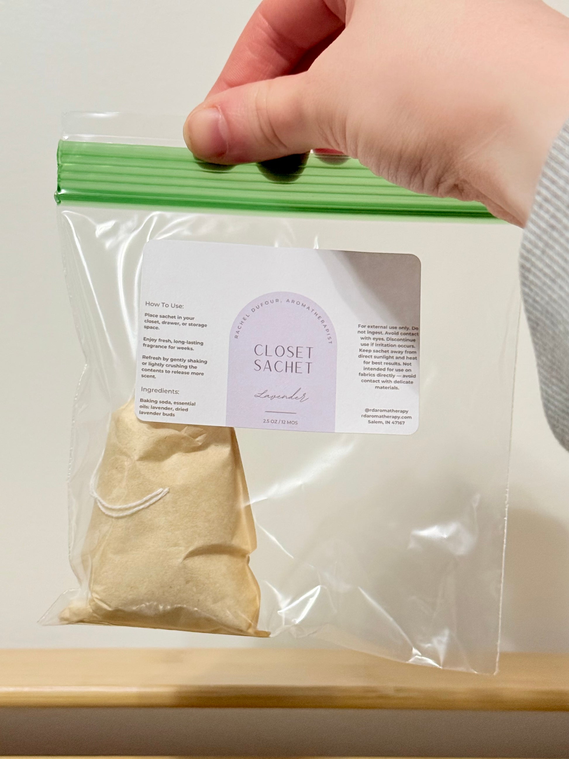 Hand holding a clear plastic bag with a closet sachet labeled 'Lavender' on a white background.