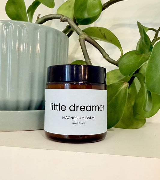 Jar of 'little dreamer' magnesium balm with a plant in the background